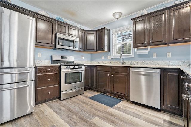 kitchen with appliances with stainless steel finishes, sink, dark brown cabinetry, and light hardwood / wood-style flooring