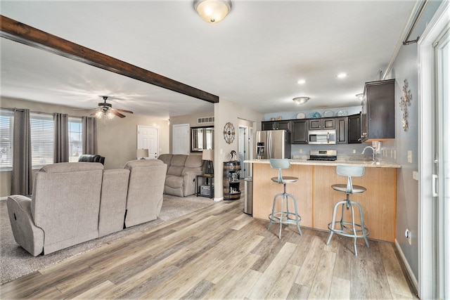 kitchen featuring a kitchen breakfast bar, stainless steel appliances, dark brown cabinetry, kitchen peninsula, and light wood-type flooring