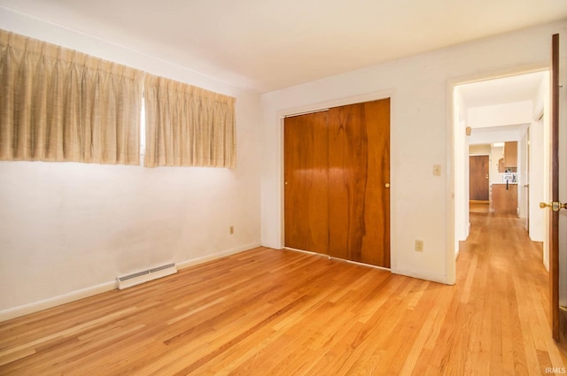 unfurnished bedroom with light hardwood / wood-style floors, a closet, and baseboard heating