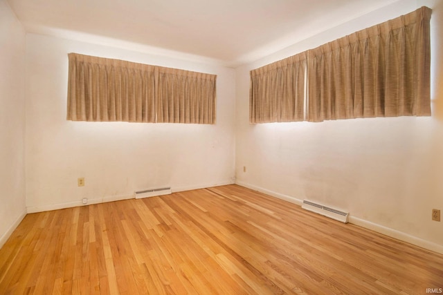 spare room featuring baseboard heating and light hardwood / wood-style flooring