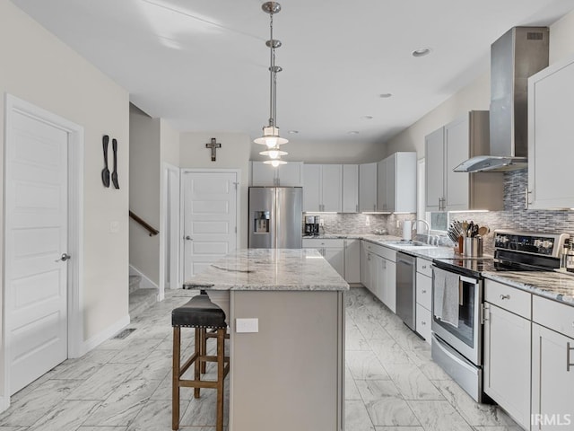 kitchen featuring sink, appliances with stainless steel finishes, hanging light fixtures, a center island, and wall chimney exhaust hood