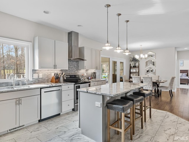 kitchen featuring stainless steel appliances, light stone counters, a kitchen island, decorative light fixtures, and wall chimney exhaust hood