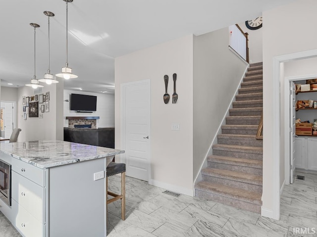 kitchen with hanging light fixtures, a kitchen island, a breakfast bar area, and light stone counters