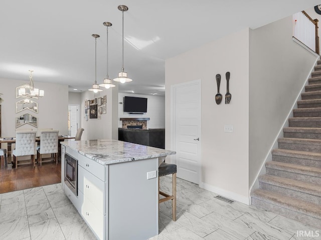 kitchen featuring a breakfast bar, stainless steel microwave, a kitchen island, a brick fireplace, and decorative light fixtures