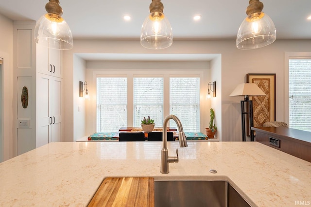 kitchen with hanging light fixtures, light stone countertops, and sink