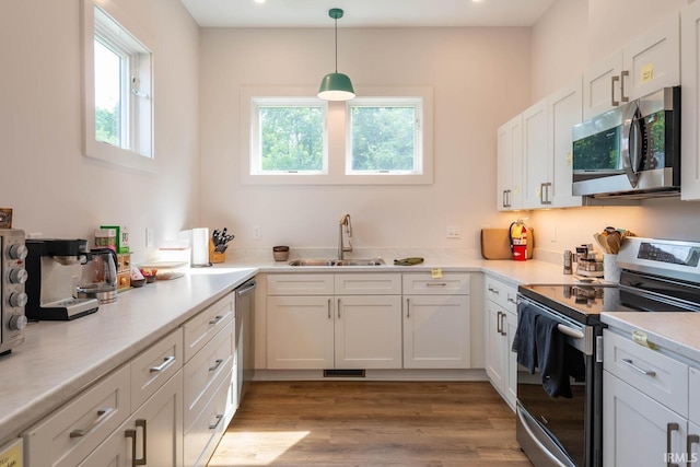 kitchen with sink, white cabinetry, hanging light fixtures, appliances with stainless steel finishes, and light hardwood / wood-style floors