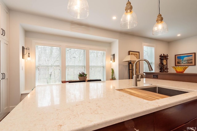 kitchen featuring plenty of natural light, sink, light stone counters, and decorative light fixtures