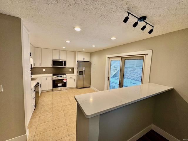 kitchen featuring a peninsula, appliances with stainless steel finishes, backsplash, and white cabinets