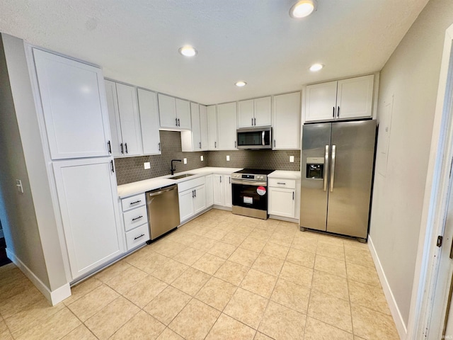 kitchen featuring tasteful backsplash, stainless steel appliances, light countertops, white cabinetry, and a sink