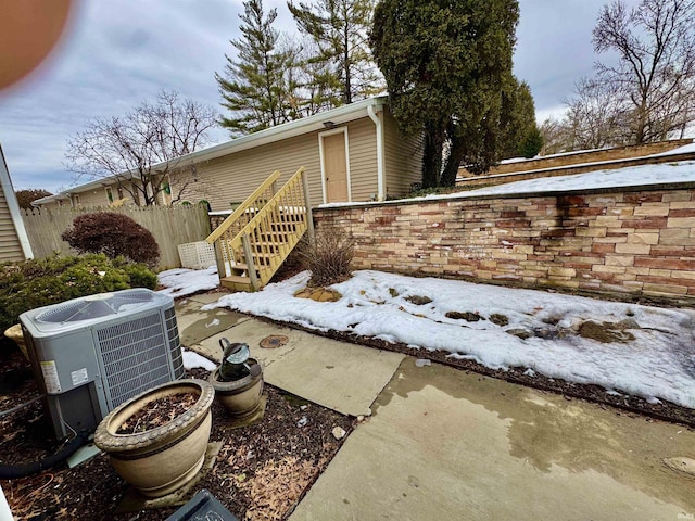 snow covered property with central air condition unit and fence