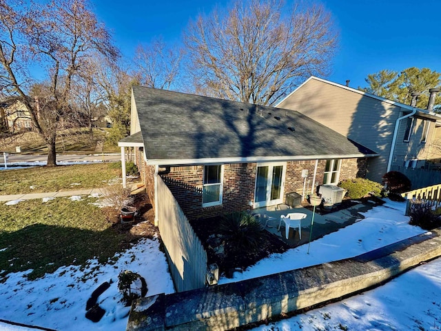 snow covered property with brick siding and a shingled roof