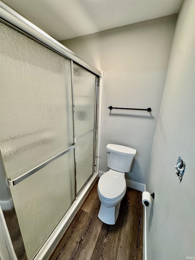 bathroom with toilet, a stall shower, baseboards, and wood finished floors