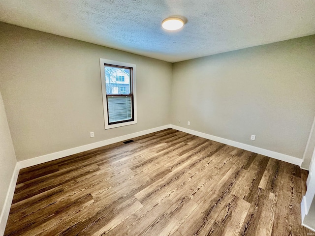 unfurnished room featuring a textured ceiling, wood finished floors, visible vents, and baseboards