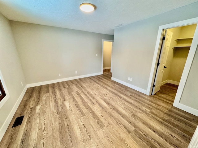 unfurnished bedroom featuring a walk in closet, visible vents, a textured ceiling, light wood-type flooring, and baseboards