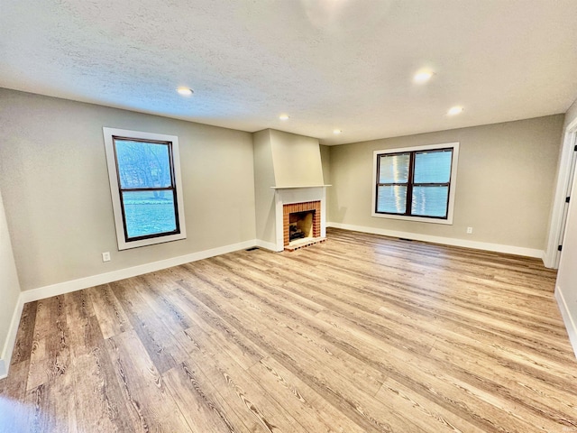 unfurnished living room with recessed lighting, a brick fireplace, a textured ceiling, light wood-type flooring, and baseboards