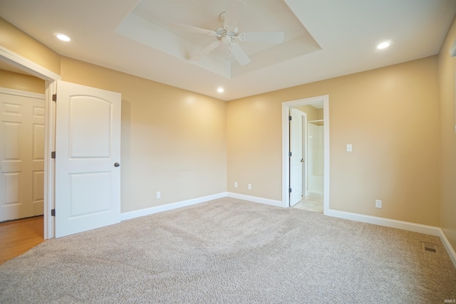 empty room featuring ceiling fan, a tray ceiling, and light carpet