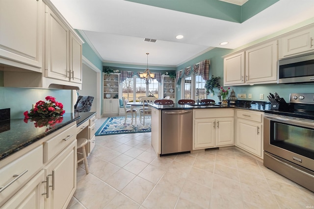 kitchen with pendant lighting, sink, appliances with stainless steel finishes, a notable chandelier, and cream cabinetry