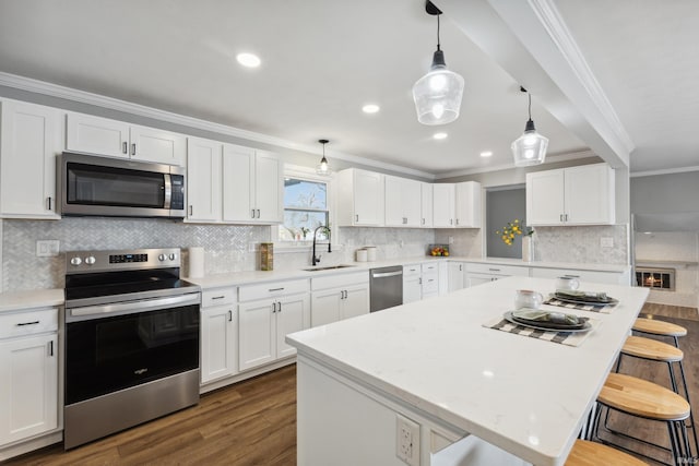 kitchen with appliances with stainless steel finishes, sink, white cabinets, and a kitchen breakfast bar