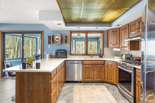 kitchen with appliances with stainless steel finishes, sink, decorative backsplash, kitchen peninsula, and light wood-type flooring