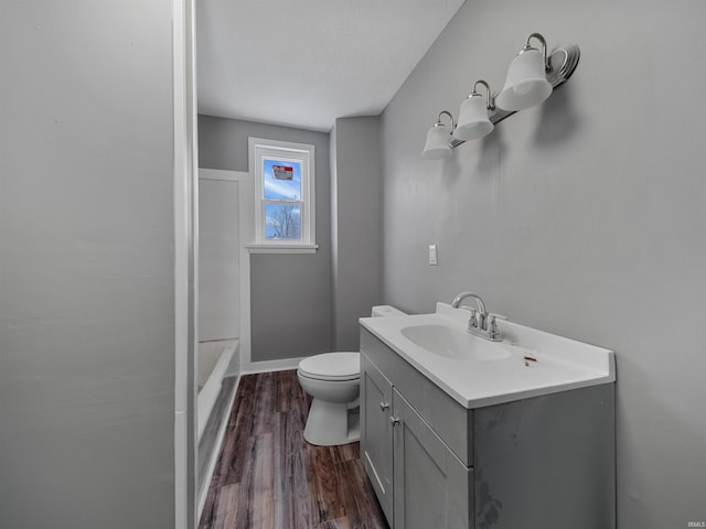 bathroom with hardwood / wood-style flooring, vanity, toilet, and a bath