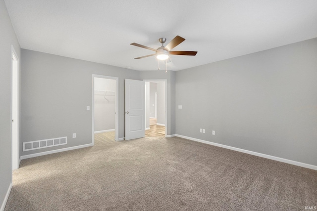 unfurnished bedroom with a walk in closet, a closet, ceiling fan, and carpet flooring