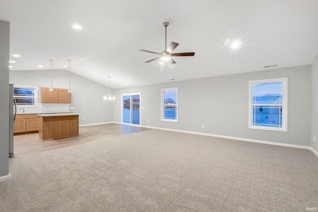 unfurnished living room with light carpet, ceiling fan with notable chandelier, and vaulted ceiling