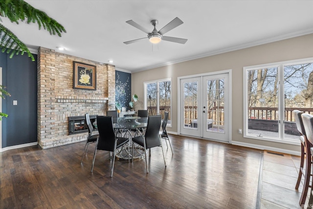 dining room featuring dark hardwood / wood-style flooring, ornamental molding, ceiling fan, a brick fireplace, and french doors