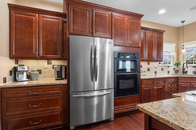 kitchen with pendant lighting, sink, stainless steel refrigerator, black double oven, and light stone countertops