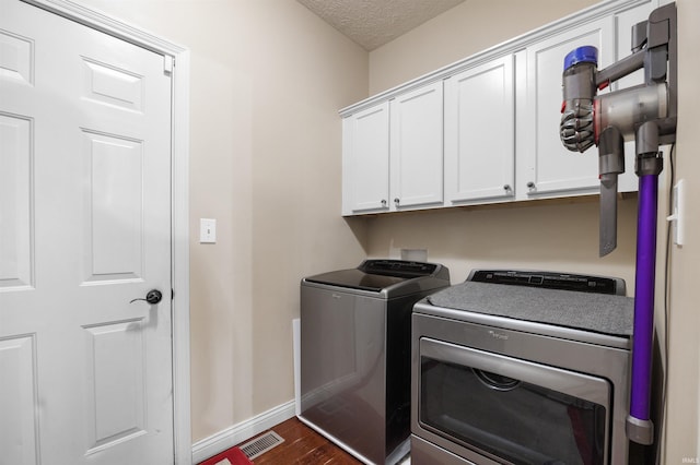 clothes washing area featuring dark wood-type flooring, cabinets, separate washer and dryer, and a textured ceiling