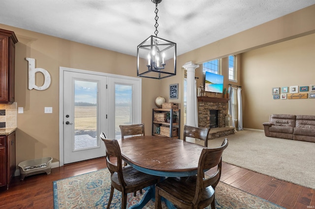 dining room featuring a stone fireplace, dark hardwood / wood-style flooring, and ornate columns