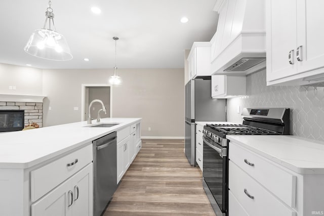 kitchen featuring premium range hood, white cabinetry, hanging light fixtures, appliances with stainless steel finishes, and a center island with sink