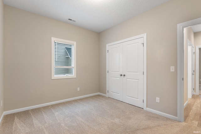 unfurnished bedroom with light colored carpet, a closet, and a textured ceiling