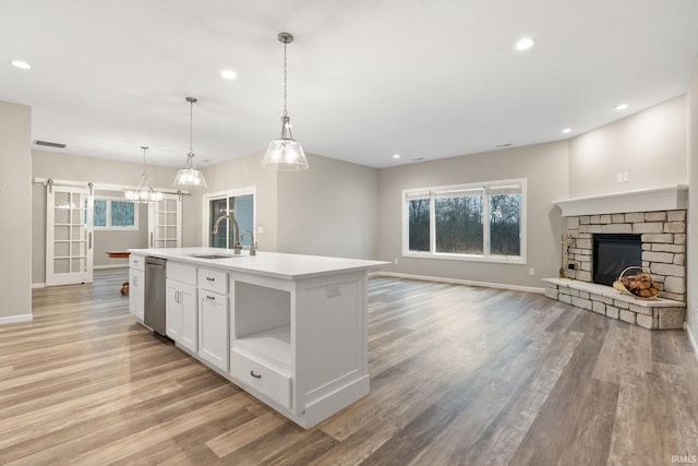 kitchen with hanging light fixtures, stainless steel dishwasher, a barn door, a kitchen island with sink, and white cabinets