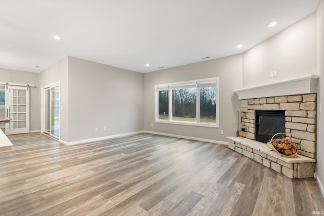 unfurnished living room featuring a stone fireplace, light hardwood / wood-style floors, and a barn door