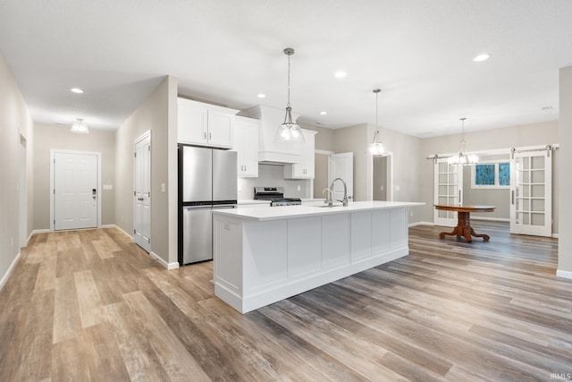 kitchen featuring sink, light hardwood / wood-style flooring, appliances with stainless steel finishes, white cabinetry, and a kitchen island with sink