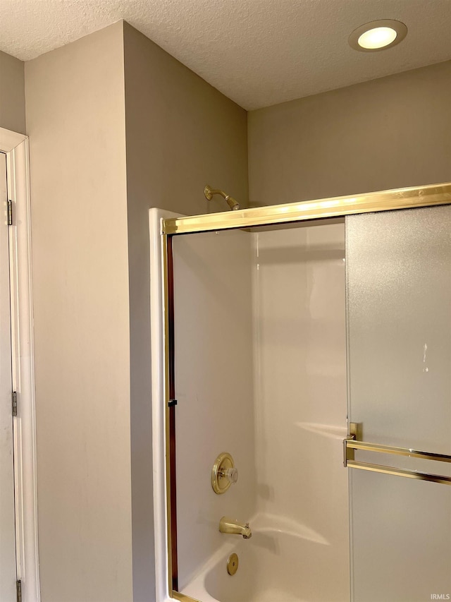 bathroom featuring bath / shower combo with glass door and a textured ceiling