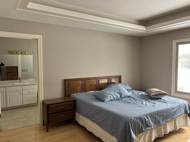 bedroom featuring ensuite bathroom, sink, light hardwood / wood-style flooring, a textured ceiling, and a tray ceiling