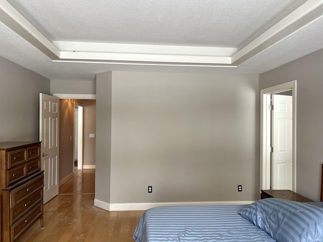 bedroom with a raised ceiling, a textured ceiling, and light wood-type flooring