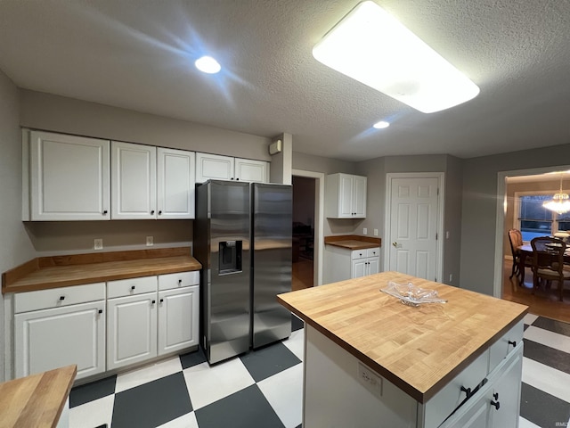 kitchen with wood counters, a center island, stainless steel fridge with ice dispenser, a textured ceiling, and white cabinets