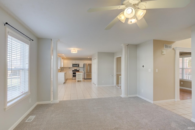 unfurnished living room with light colored carpet, ceiling fan, and ornate columns