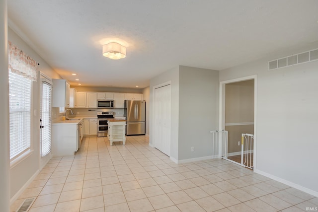 kitchen with stainless steel appliances, light tile patterned flooring, sink, and white cabinets