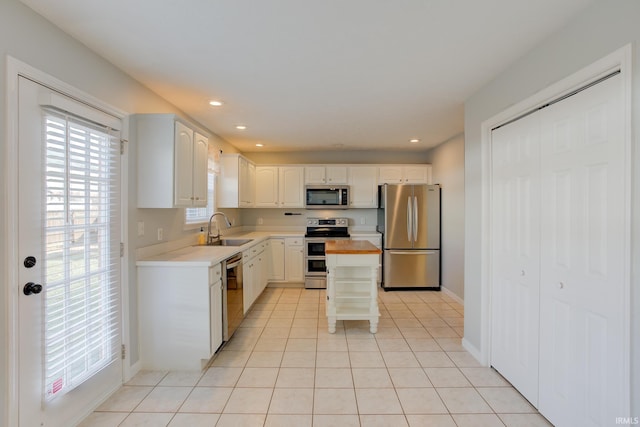 kitchen with sink, appliances with stainless steel finishes, white cabinets, a kitchen island, and light tile patterned flooring