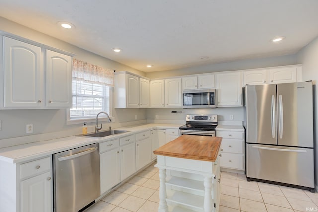 kitchen featuring light tile patterned flooring, appliances with stainless steel finishes, white cabinetry, sink, and butcher block counters