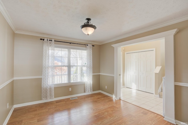 empty room with ornamental molding, a textured ceiling, and light wood-type flooring