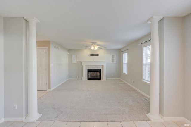 unfurnished living room with ceiling fan, a tiled fireplace, light carpet, and ornate columns