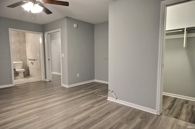 unfurnished bedroom with hardwood / wood-style floors, connected bathroom, a walk in closet, ceiling fan, and a closet