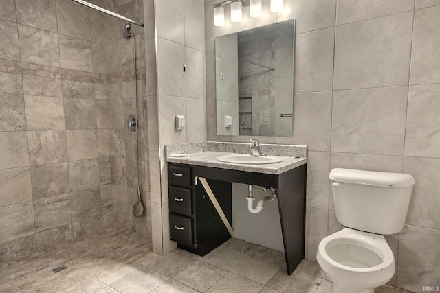 bathroom with tile walls, vanity, toilet, and a tile shower