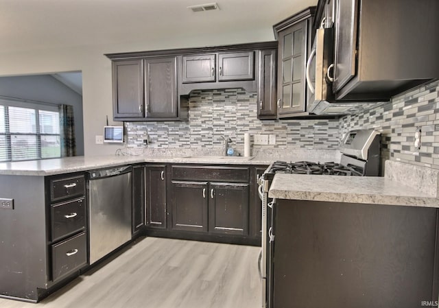 kitchen with sink, appliances with stainless steel finishes, backsplash, dark brown cabinets, and kitchen peninsula