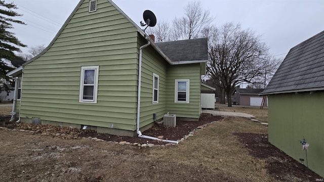 view of side of home featuring cooling unit and a shingled roof