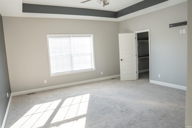 unfurnished bedroom with a walk in closet, a raised ceiling, light colored carpet, and a closet